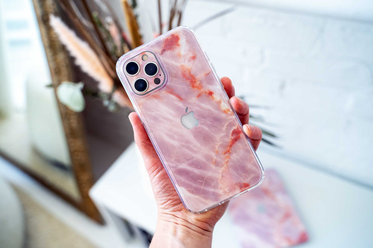 Hand holding an iPhone 14 with a protective clear case featuring a stylish pink and white marble pattern.