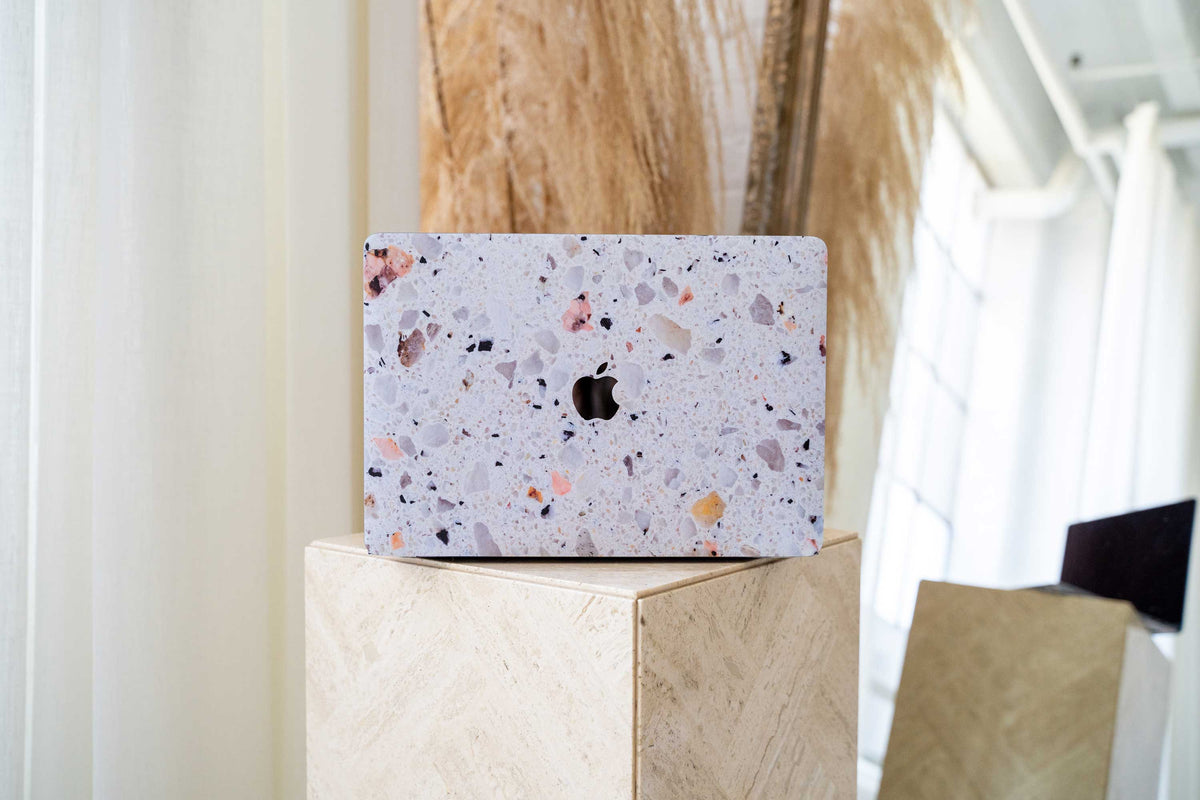 MacBook with a speckled terrazzo-patterned hard shell case resting on a stone pedestal.