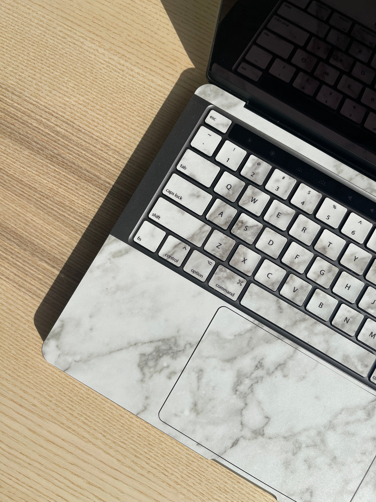 MacBook keyboard and trackpad covered in a sleek, white marble-patterned adhesive skin on a wooden desk.